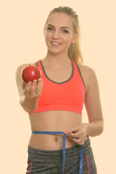 Joven adolescente feliz sonriendo mientras que da manzana roja y medir la cintura listo para el gimnasio —  Fotos de Stock