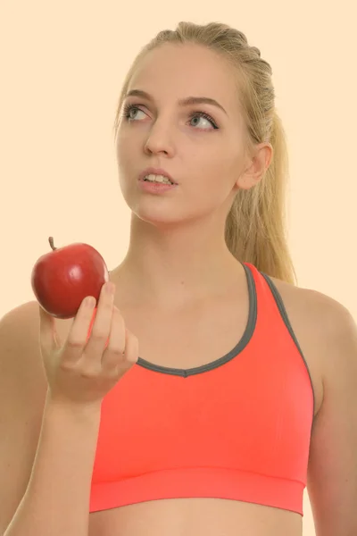 Rosto de jovem bela adolescente segurando maçã vermelha enquanto pensa pronto para ginásio — Fotografia de Stock