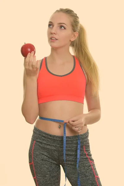 Genç ve güzel bir kız kırmızı elmayı tutarken düşünürken ve belini ölçerken spor salonuna hazır. — Stok fotoğraf