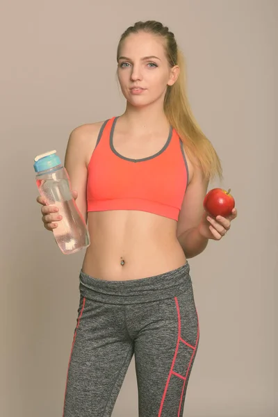 Genç ve güzel bir kız elinde su şişesi ve kırmızı elmayla spor salonuna hazır. — Stok fotoğraf