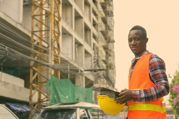 Jonge zwarte Afrikaanse man bouwvakker met klembord en harde hoed op bouwplaats — Stockfoto