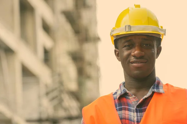 Joven feliz negro africano trabajador de la construcción sonriendo en el sitio de construcción —  Fotos de Stock