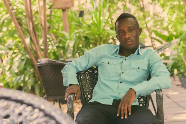 Joven hombre africano negro sentado en la cafetería al aire libre rodeado de naturaleza —  Fotos de Stock