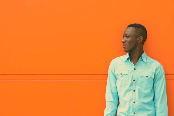 Profile view of young black African man thinking while looking at distance against orange painted wall