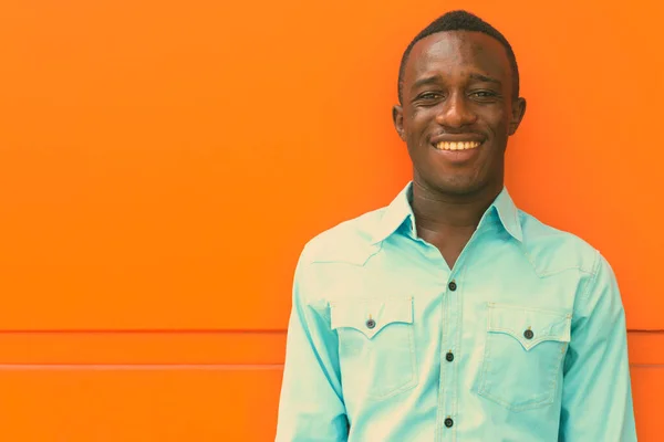 Young happy black African man smiling while leaning against orange painted wall