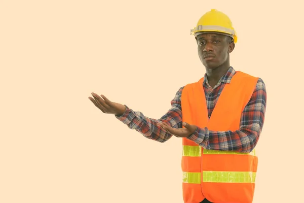 Estúdio tiro de jovem negro africano trabalhador da construção mostrando algo — Fotografia de Stock