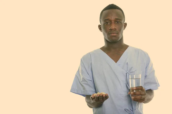 Estudio de un joven hombre africano negro sosteniendo tabletas vitamínicas y un vaso de agua —  Fotos de Stock