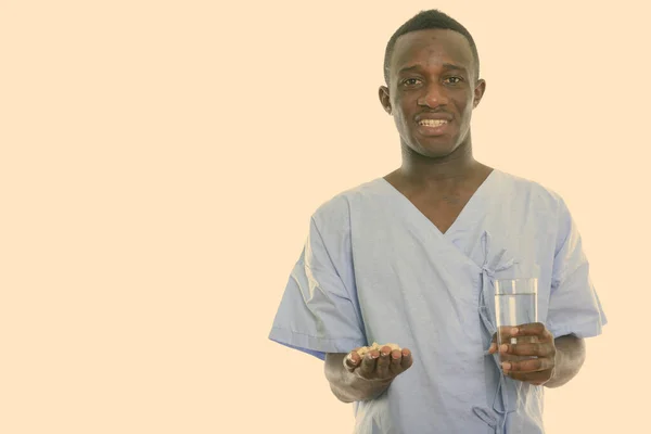 Estudio de disparo de joven hombre africano negro feliz sonriendo mientras sostiene tabletas de vitaminas y un vaso de agua —  Fotos de Stock