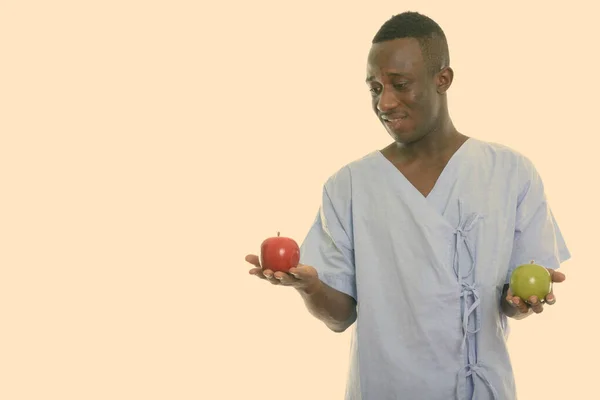 Estudio disparo de joven feliz negro africano hombre paciente sonriendo mientras mira la manzana roja y la celebración de manzana verde —  Fotos de Stock