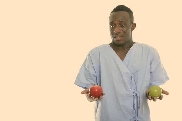 Studio strzał młody czarny Afrykanin mężczyzna pacjent patrząc mylić trzymając czerwone jabłko i zielone jabłko — Zdjęcie stockowe