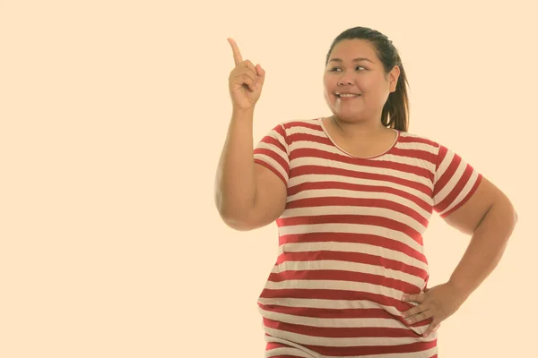 Studio skott av ung glad fet asiatisk kvinna ler och tänker samtidigt peka finger upp — Stockfoto
