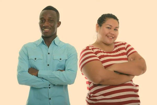 Happy young fat Asian woman and young black African man smiling with arms crossed together — Stock Photo, Image