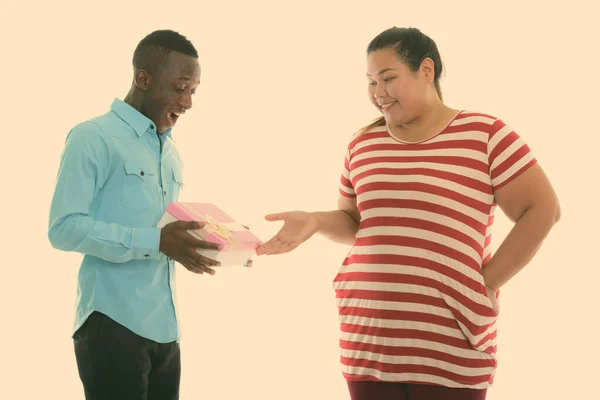 Szczęśliwy młody tłuszcz Azji kobieta dając prezent pudełko dla młody czarny Afrykanin mężczyzna uśmiechając się i patrząc zaskoczony — Zdjęcie stockowe