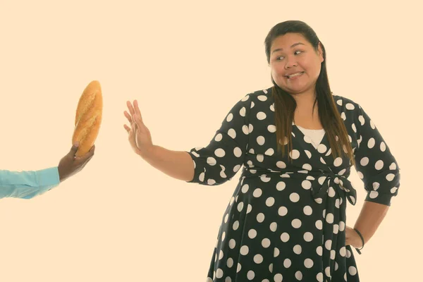Studio shot of young happy fat Asian woman smiling while showing stop hand sign with bread