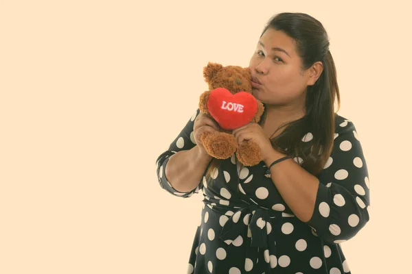 Studio záběr mladé tlusté asijské žena držení a líbání medvídek se srdcem a láska znamení — Stock fotografie