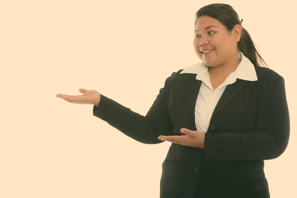 Studio shot of young happy fat Asian businesswoman smiling and showing something — Stock Photo, Image
