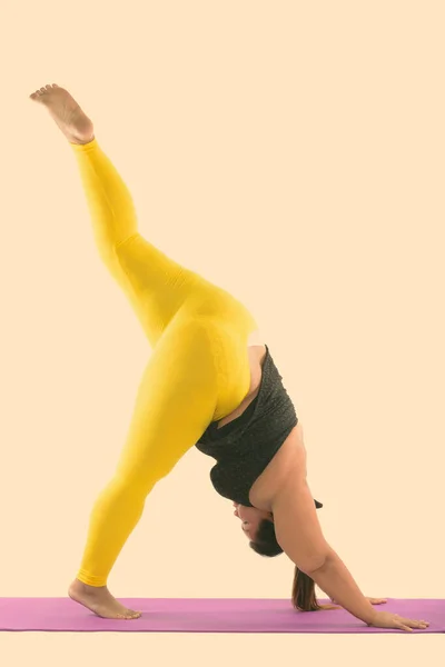 Studio shot of young fat Asian woman raising one foot up while doing yoga poses — Stock Photo, Image