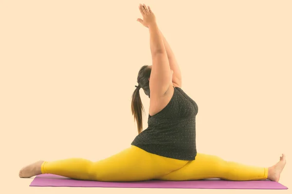 Studio shot of young fat Asian woman spitting her legs while reaching up with both hands