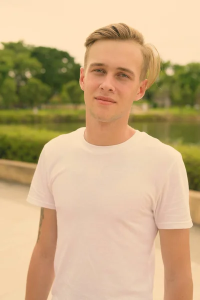 Jovem homem bonito com cabelo loiro relaxante no parque — Fotografia de Stock
