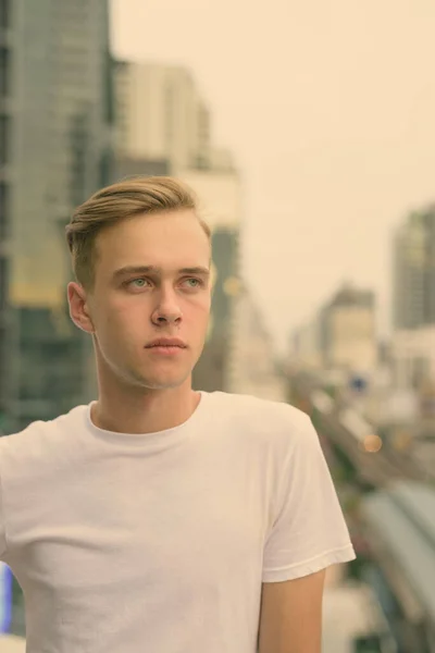 Mladý pohledný muž s blond vlasy proti pohledu na město — Stock fotografie