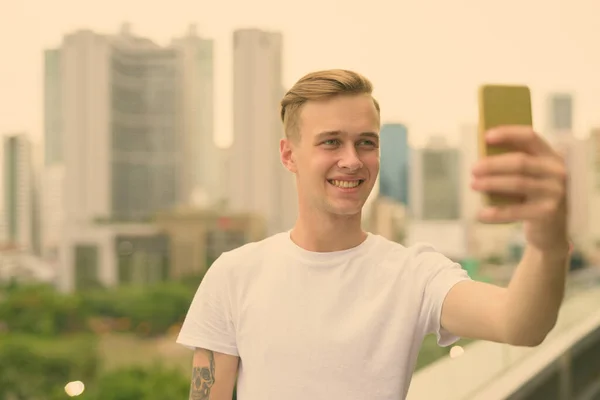 Young handsome man with blond hair against view of the city — Stock Photo, Image