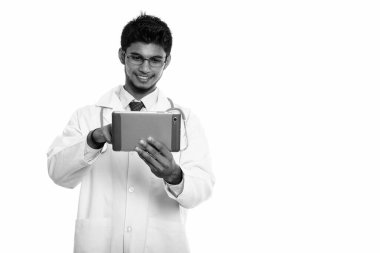 Dijital tablet kullanırken gülümseyen genç Hintli doktorun stüdyo fotoğrafı.