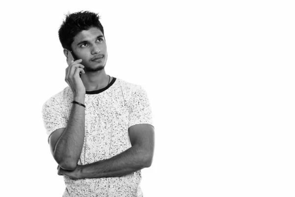 Estúdio tiro de jovem indiano bonito falando no telefone celular enquanto pensa — Fotografia de Stock