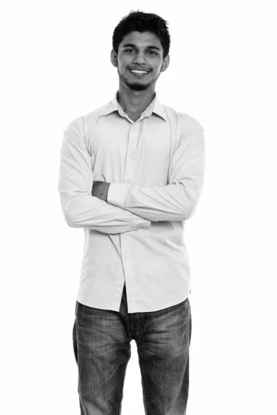 Студийный снимок молодого счастливого индийца, улыбающегося и стоящего со скрещенными руками — стоковое фото
