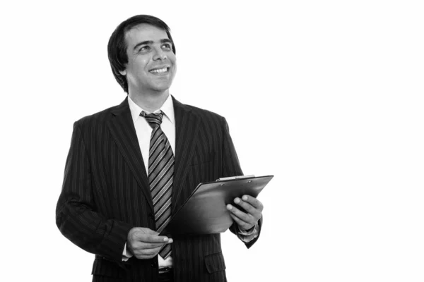 Estúdio tiro de jovem feliz empresário persa sorrindo e segurando prancheta enquanto pensa — Fotografia de Stock