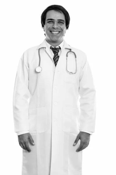 Studio shot of young happy Persian man doctor souriant tout en se tenant debout et portant des lunettes — Photo