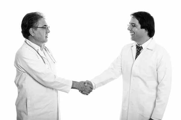 Profile view of happy young and senior Persian man doctor smiling and shaking hands — Stock Photo, Image