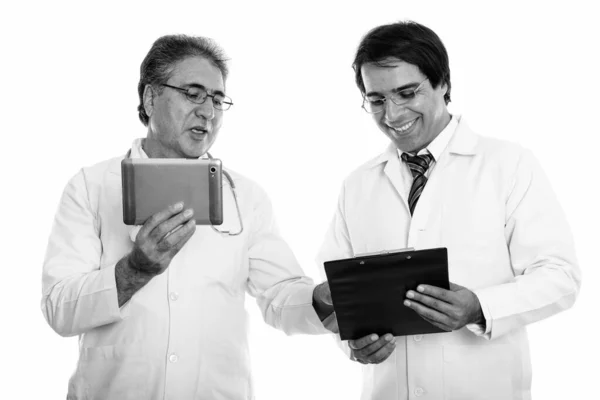 Estúdio tiro de feliz jovem e sênior persa homem médico sorrindo enquanto segurando tablet digital e leitura na área de transferência — Fotografia de Stock