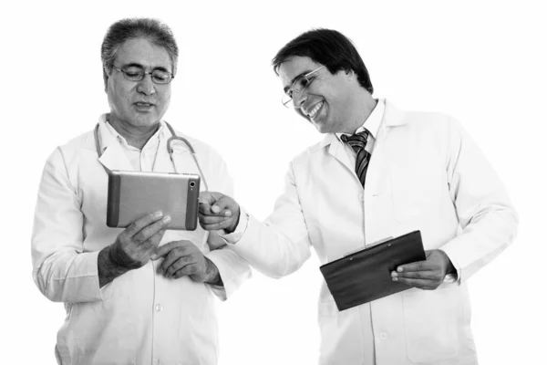 Студийный снимок счастливого молодого и старшего персидского врача, улыбающегося при использовании цифрового планшета и держащего планшет — стоковое фото