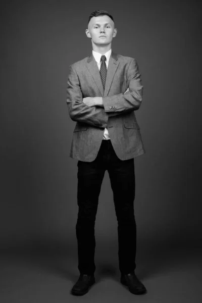 Jovem empresário vestindo terno contra fundo cinza — Fotografia de Stock