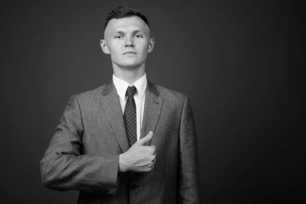 Joven hombre de negocios que usa traje contra fondo gris —  Fotos de Stock