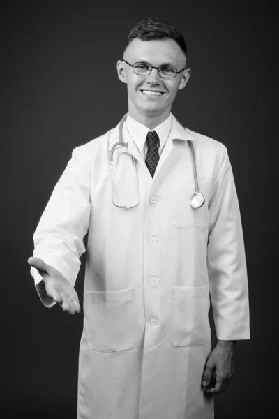 Joven doctor vistiendo anteojos sobre fondo gris — Foto de Stock