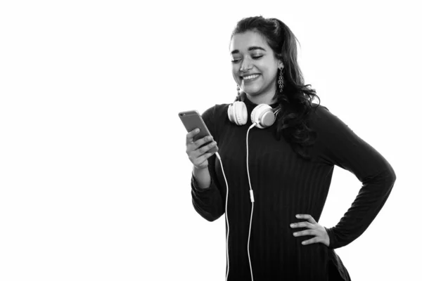 Giovane donna indiana felice sorridente mentre indossa le cuffie intorno al collo durante l'utilizzo del telefono cellulare — Foto Stock