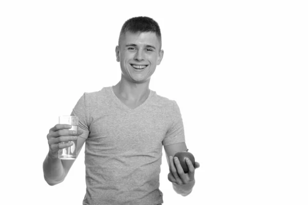 Joven hombre caucásico feliz sonriendo mientras sostiene un vaso de agua y manzana — Foto de Stock