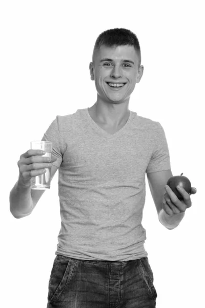 Jeune homme heureux caucasien souriant tout en tenant un verre d'eau et de pomme — Photo