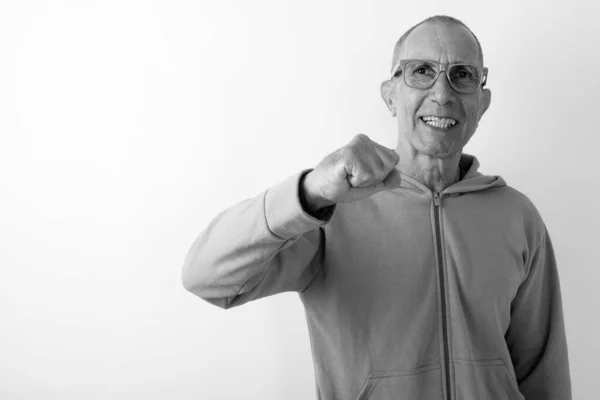 Estúdio tiro de feliz careca sênior sorrindo enquanto usava óculos com punho levantado contra fundo branco — Fotografia de Stock