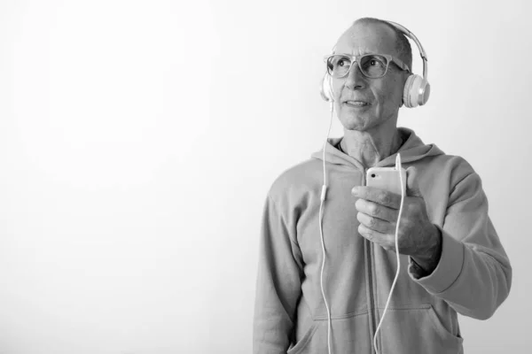 Στιγμιότυπο στούντιο του φαλακρού ηλικιωμένου άνδρα που κρατά το κινητό τηλέφωνο, ενώ σκέφτεται και να ακούτε μουσική με γυαλιά ηλίου σε λευκό φόντο — Φωτογραφία Αρχείου