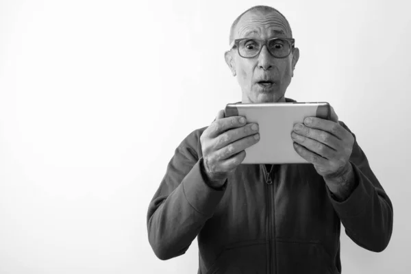 Studio shot van geschokte kale senior man met behulp van digitale tablet terwijl het dragen van een bril tegen een witte achtergrond — Stockfoto