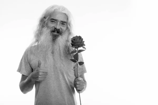 Estudio de tiro de hombre barbudo alto feliz sonriendo mientras sostiene rosa y dando pulgar arriba listo para el día de San Valentín —  Fotos de Stock