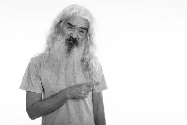 Studio shot of senior bearded man looking disgusted while pointing to the side — Stock Photo, Image