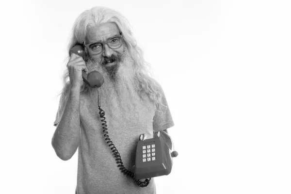 Studio shot van gelukkig senior bebaarde man glimlachend terwijl het praten op oude telefoon — Stockfoto
