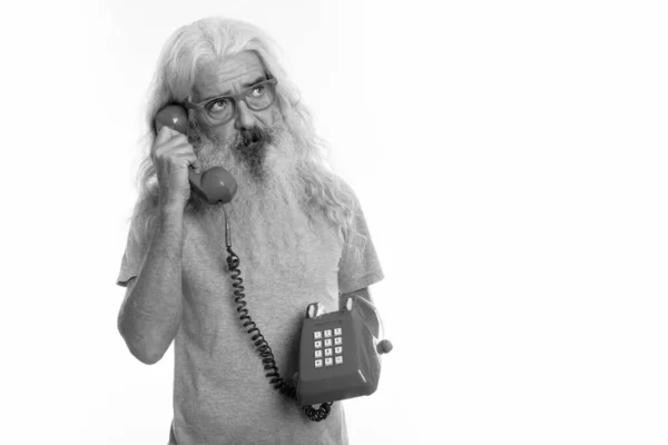 Studio shot van senior bebaarde man denken tijdens het praten op oude telefoon — Stockfoto