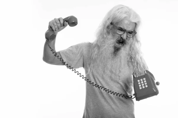 Studio shot of senior barbu homme regardant en colère et criant tout en tenant vieux téléphone — Photo