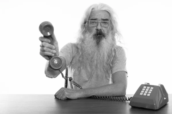 Studio shot van senior bebaarde man geven oude telefoon op houten tafel — Stockfoto
