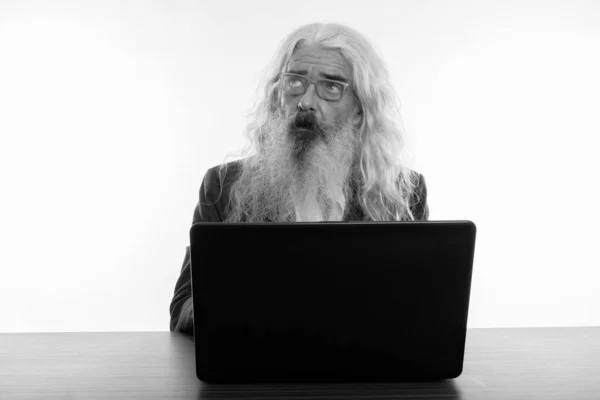 Plan studio d'un homme d'affaires barbu âgé réfléchissant et levant les yeux tout en utilisant un ordinateur portable sur une table en bois — Photo