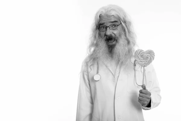 Studio colpo di felice anziano barbuto uomo medico sorridente mentre tiene a forma di cuore lecca-lecca — Foto Stock